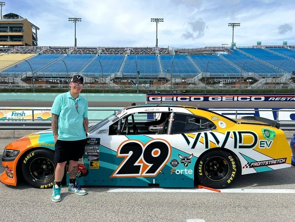 Joe R. Wells standing beside the teal, orange and yellow No. 29 Vivid EV Ford on pit road at Homestead-Miami Speedway
