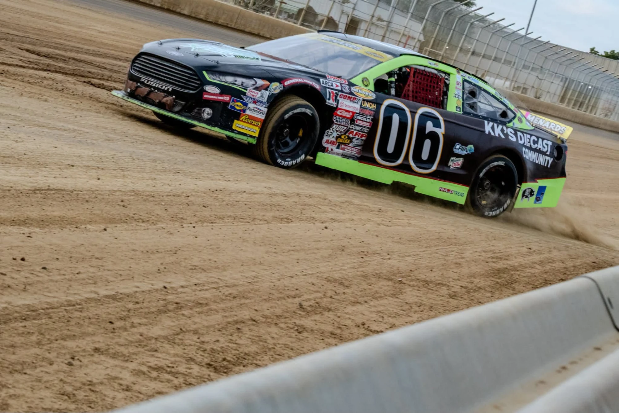 Black and green No. 06 KK's Diecast Community Ford sliding on a dirt track